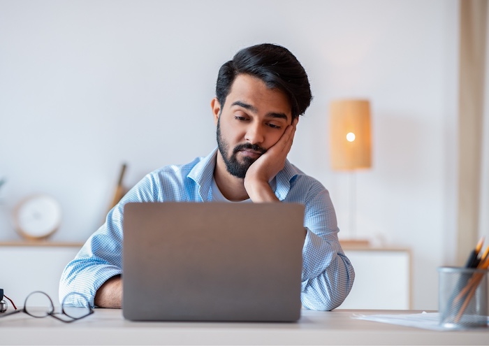 man zit oververmoeid aan zijn laptop